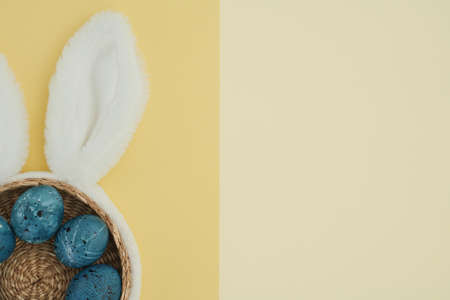 Easter composition on a two-color yellow background of Easter eggs in a basket and bunny ears as a...