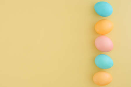 Minimalistic Easter composition of pastel colorful eggs in blue, yellow and pink colors on a pale yellow background. Copy space, top view, flat layの写真素材