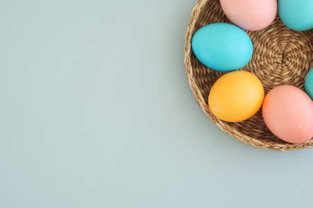 Easter composition with a wicker basket with Easter eggs painted in pastel multicolored colors on a gentle blue background with copy space, top view, flat layoutの写真素材