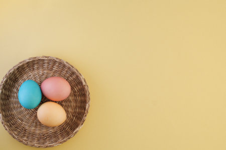 Minimalistic Easter composition with colorful Easter eggs in a wicker basket on a yellow trendy background with place for text, flat lay. Easter concept, Easter eggs painted in pastel colorsの写真素材