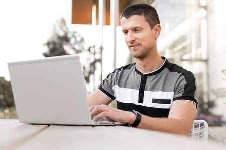 A young man or student or businessman is sitting at a table with a laptop and typing on the keyboard.の写真素材