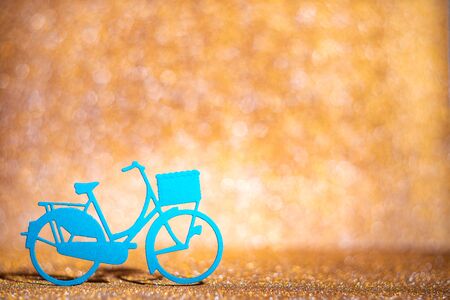 Blue paper bicycle on the gold glitter bg, Abstract holidays background. Texture, light bokeh background, Glitter lights background.の写真素材