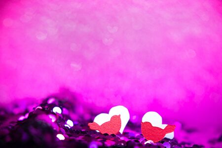 Red birds and hearts from paper sits on glitter texture, christmas or valentine's day background. Macro shot. Bright fabric with brilliant paillettes. Abstract holidays background. Texture, light bokeh background, Glitter lights background.の写真素材