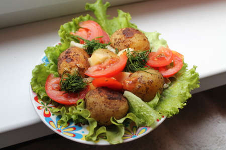 dish from young potato in reel made on grill lay on leaves of green salad and pulp red slices of tomato and dill, cheeseの写真素材