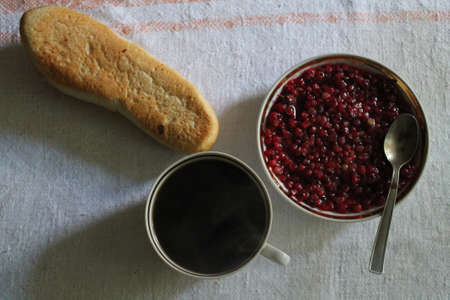 cup with black coffee, crust bun and saucer with sweet strawberry jam summer breakfastの写真素材
