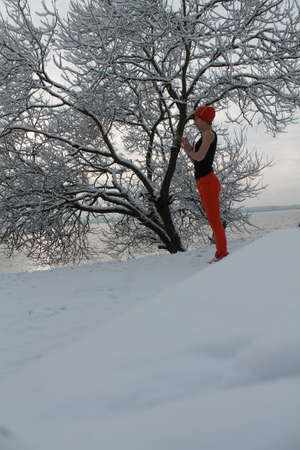 flexible tall young woman stay praying under tree on the sea shore in cold winter day