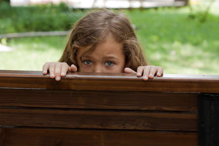 Kid Hiding Behind A BenchIn. Little Girl Six Year Old Hiding Behind A Wooden Bench In Park Summer.の写真素材