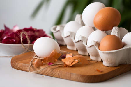 White And Brown Eggs On Wooden Cutting Board With Onion Peel On White Table At Easter.