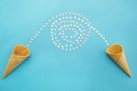 Waffle cones, cups on a blue background and candy hearts pouring from them and swirling with each...