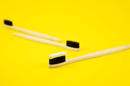 Three bamboo brushes with natural bristles and elodogic toothpaste on a yellow background. Caring for the environment. Zero waste. Proper oral careの写真素材
