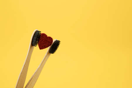Two bamboo eco brushes and a red heart on a yellow background. Place for text. Oral care, no caries.の写真素材