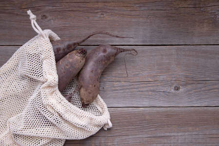 Fresh long-drawn bio beets in a cotton reusable string bag of beige color lie on a wooden table. Refusal of plastic. No waste. Place for textの写真素材