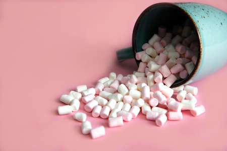 white and pink mini marshmallows, small marshmallows sprinkled from a cup, from a turquoise cup on a pink background. Place for textの写真素材