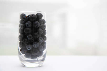 Sweet tasty bilberries in pot. fresh blueberries with a glass goblet. Blueberries in a glass on the windowsill. White curtain in the backgroundの写真素材