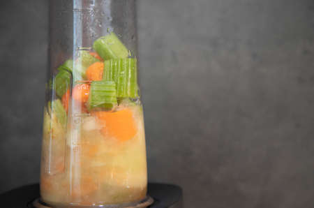 Part of the ground celery pieces, apples and carrots. Cooking smoothies in the process. Preparing a smoothie in a blender from fresh vegetables and fruits. Gray background. Raw foodの写真素材