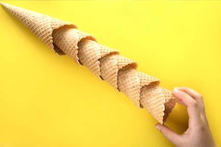 Children's hand pulls one empty waffle cup. Waffle cups lie diagonally on a yellow background and a children's hand pulls one of them.の写真素材