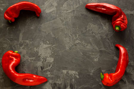 Four ugly paprikas lie at the corners of a black concrete background. Deformed red pepper on a dark background. Place for text.の写真素材