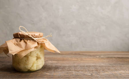 Traditional homemade fermented cauliflower in a glass jar on a wooden table. Horizontal orientation....