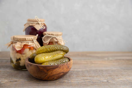 Pickled, salted, fermented cucumbers lie in a wooden bowl on a wooden table. On a squid background...
