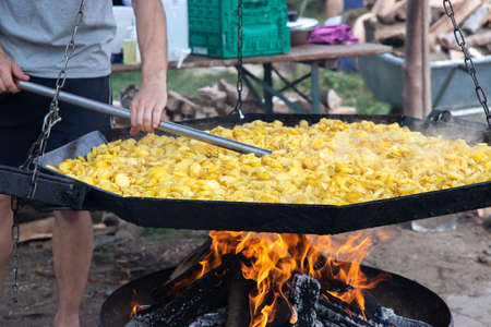 Street festival of potatoes in Germany. Traditional fried potatoes with onions over an open fire in a huge frying pan. A man is stirring potatoes.の写真素材