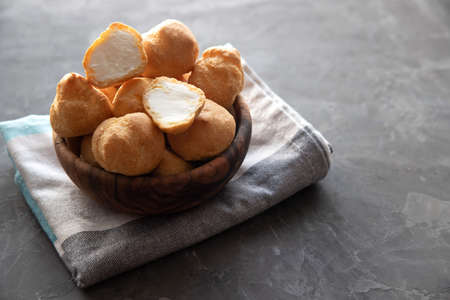 Small round whole eclairs and one cut in half lie in a wooden bowl and stand on a gray dining napkin on a dark concrete background. Copy space.の写真素材