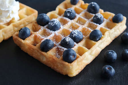 Fresh Belgian or Viennese waffles with blueberries closeup on a black background Dessert for breakfastの写真素材