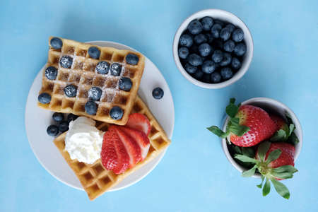Viennese waffles on a white porcelain plate with fresh strawberries and blueberries and icing sugar....