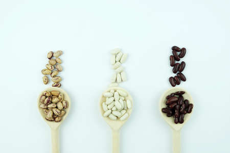 Different varieties of beans white, red and Pinto, lie on wooden spoons on a white background. Copy spaceの写真素材