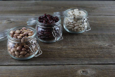 Three different varieties of beans in glass jars on an old wooden table. Colorful beans. Legumes as a source of protein. Place for textの写真素材