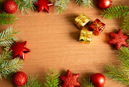 green pine branches with red New Year's toys, balls and stars, together with gold-colored gift boxes, lie on a wooden brown table. Place for text. Christmas and holidays concept.の写真素材