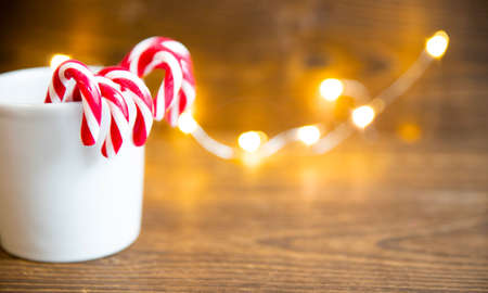 A beige glass with New Year's sweets in the form of a cane stands on an old wooden table in the...