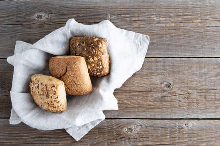 Three fresh buns with sunflower seeds, chia, oatmeal lie on a beige linen napkin. Wood background....