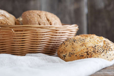 Freshly baked buns in a wicker basket and one bun next to it on a wooden background. Homebaked bread. Bread in the bakery. Bakery products.の写真素材