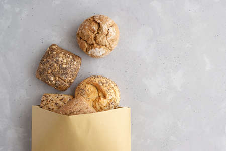 Different fresh buns, bread spilled out of a paper bag on a gray background. Buns from the bakery....