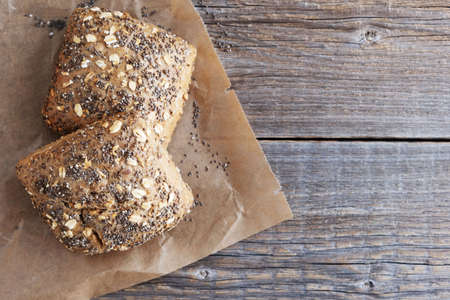 Two rye freshly baked buns with sunflower seeds, chia and oatmeal flakes lie on baking paper on a wooden rustic table. Copy Space.の写真素材