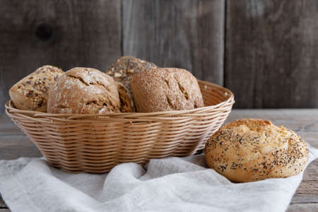 Different varieties of bread and bun lie in a wicker basket and next to them are a wheat roll and a linen table napkin. Rye, spelled, whole grain baked goods with sunflower and chia seedsの写真素材