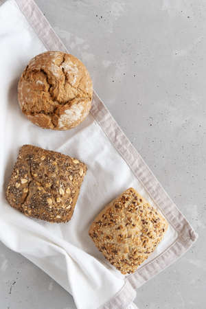 Three fresh rye, whole grain buns on a linen napkin on a concrete gray table. Buns from the bakery. Place for text.の写真素材