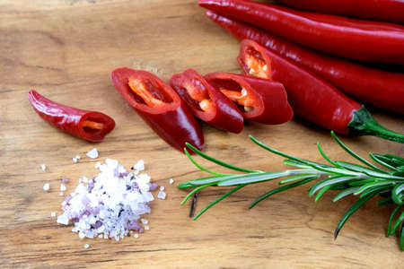 Closeup of hot red pepper chilli pods on a wooden board with a sprig of fresh rosemary and white and purple sea saltの写真素材