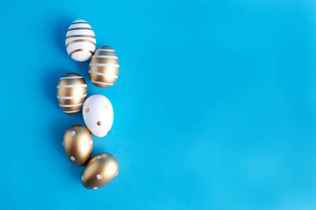 Easter eggs white and gold, gold stripes lie in a row on a blue background. Place for text. Easter concept. Easter spring holiday.の写真素材