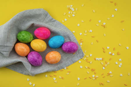 Easter eggs painted in different colors lie on a light linen napkin on a yellow background and Easter sweets are scattered nearby.の写真素材