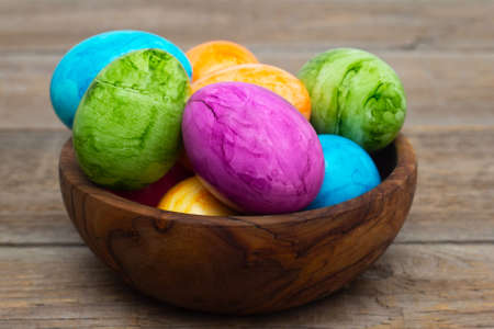 Easter colored eggs in a wooden bowl stand on a wooden table. Close-up. Easter holiday.