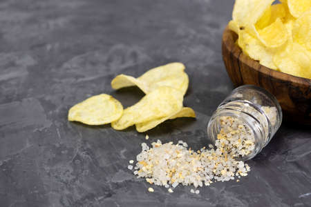 Sea salt with garlic is scattered on a black background and slices of chips are nearby. Copy space.の写真素材