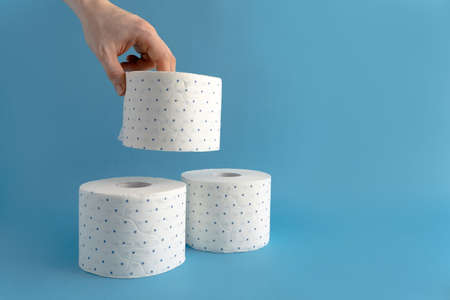 A male hand takes a roll of white toilet paper in a blue dot. Blue background. Place for text. Lack of toilet paperの写真素材
