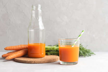 A glass bottle with fresh carrot juice on a cork stand and a glass with juice and a cocktail straw nearby. In the background a bunch of fresh carrots. Place for text.の写真素材