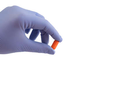 A hand in a blue medical glove holds with his fingers an orange tablet, a pill on a white background. Copy space. Medical concept. The choice of treatment.の写真素材