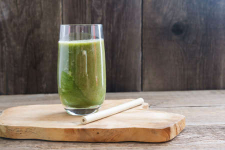 A glass of bleached celery, banana and basil smoothie next to a reusable bamboo straw on a wooden stand against a background of old wooden boards. Place for text. Healthy vegetarian drink.の写真素材
