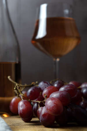 A close-up of a bunch of grapes, and in the background a bottle and a glass of pink wine are out of focus. vertical orientation.の写真素材