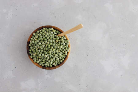 Dry green peas lie in a wooden bowl, a wooden spoon is stuck in it. Concrete gray background. Place for textの写真素材