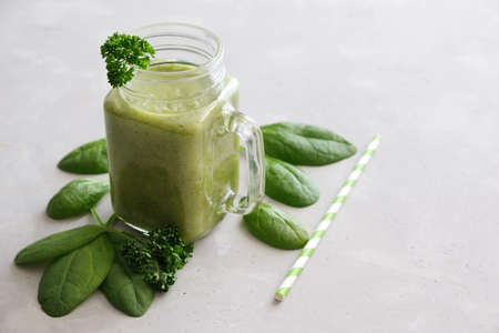 A glass mug, a glass, a glass with a zeon fresh smoothie of banana, apple, celery and spinach with leaves scattered next to it and a reusable straw on a gray concrete background. Healthy snack.の写真素材
