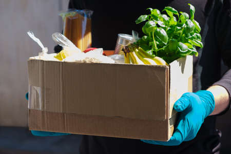 Home delivery during an epidemic. contactless delivery. Food donation. Mens hands hold a box with products.の写真素材